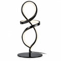 Modern black spiral table lamp on a desk with a plant and books in the background